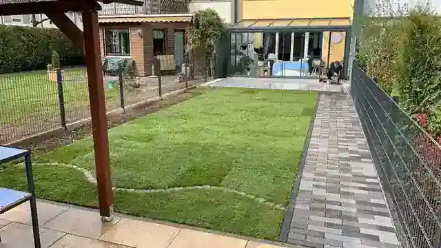 Ein gepflegter Garten mit Rasen, Ziegelweg und Zaun
