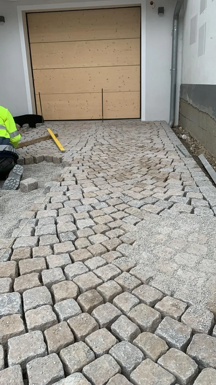 Ein Mann legt Ziegelsteine in einer Einfahrt vor einem Garagentor.